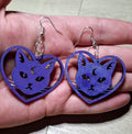 Purple cat-shaped earrings held in a hand on a light background