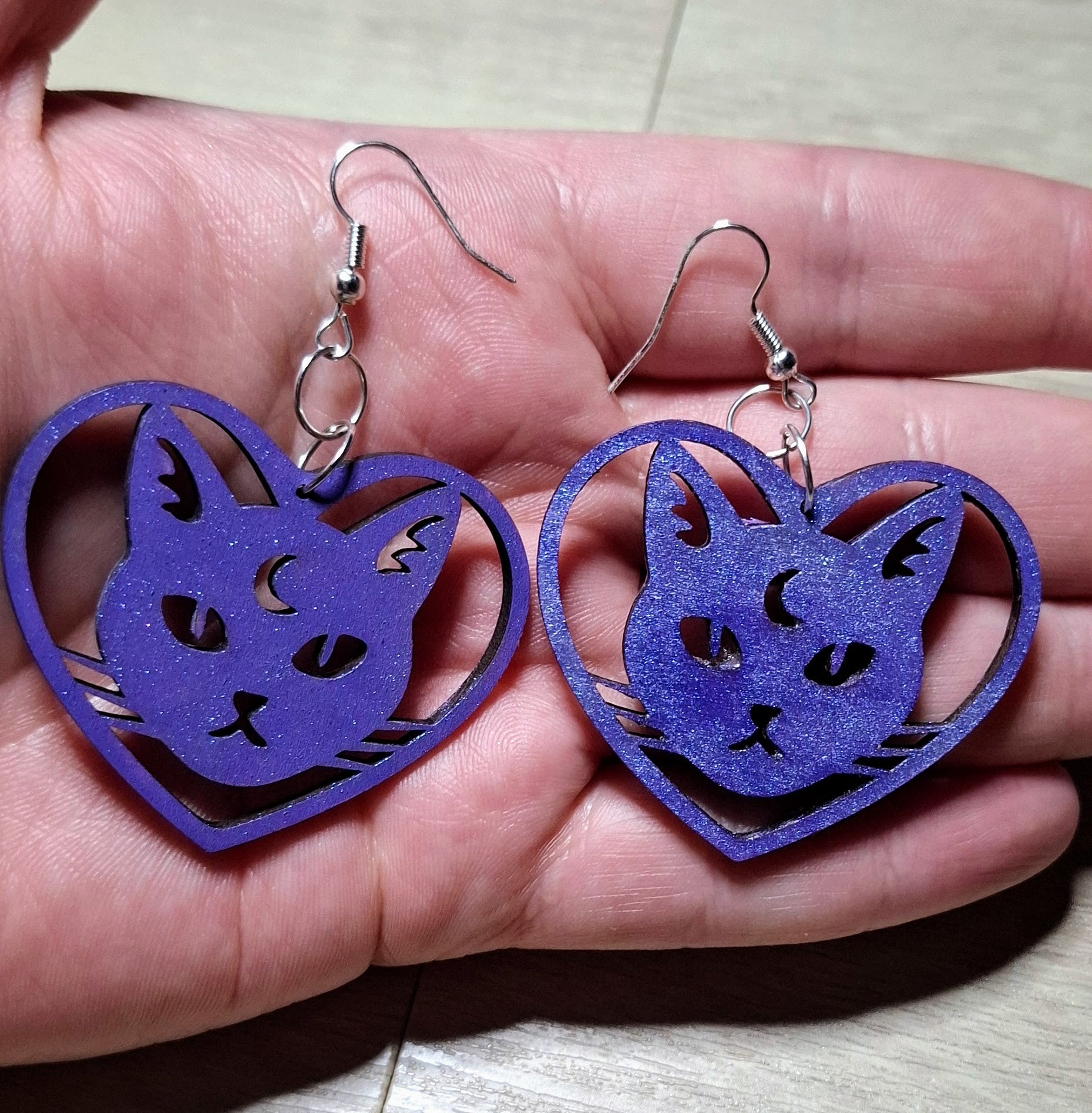 Purple cat-shaped earrings held in a hand on a light background