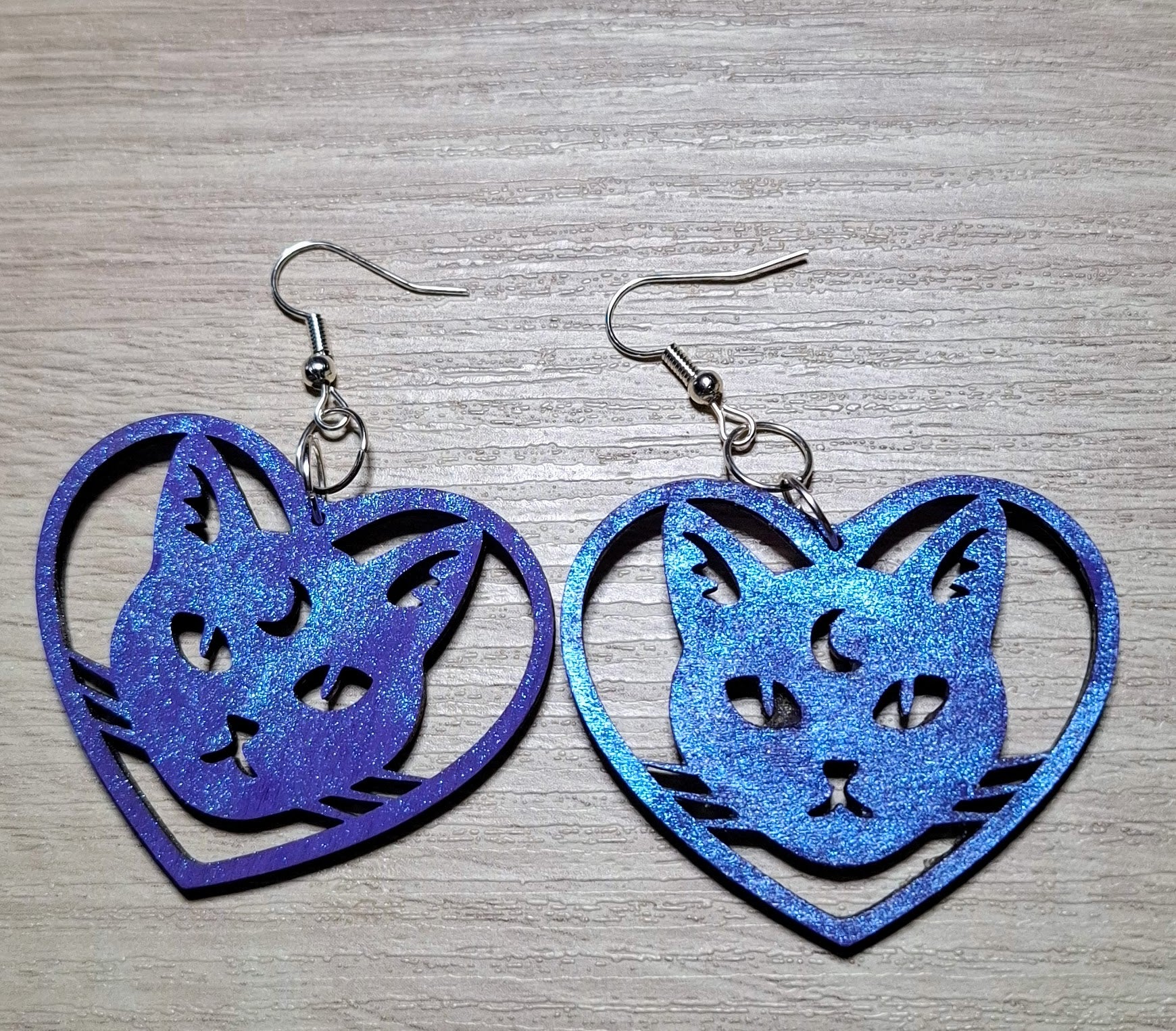 Purple glittery cat-shaped earrings on a wooden surface