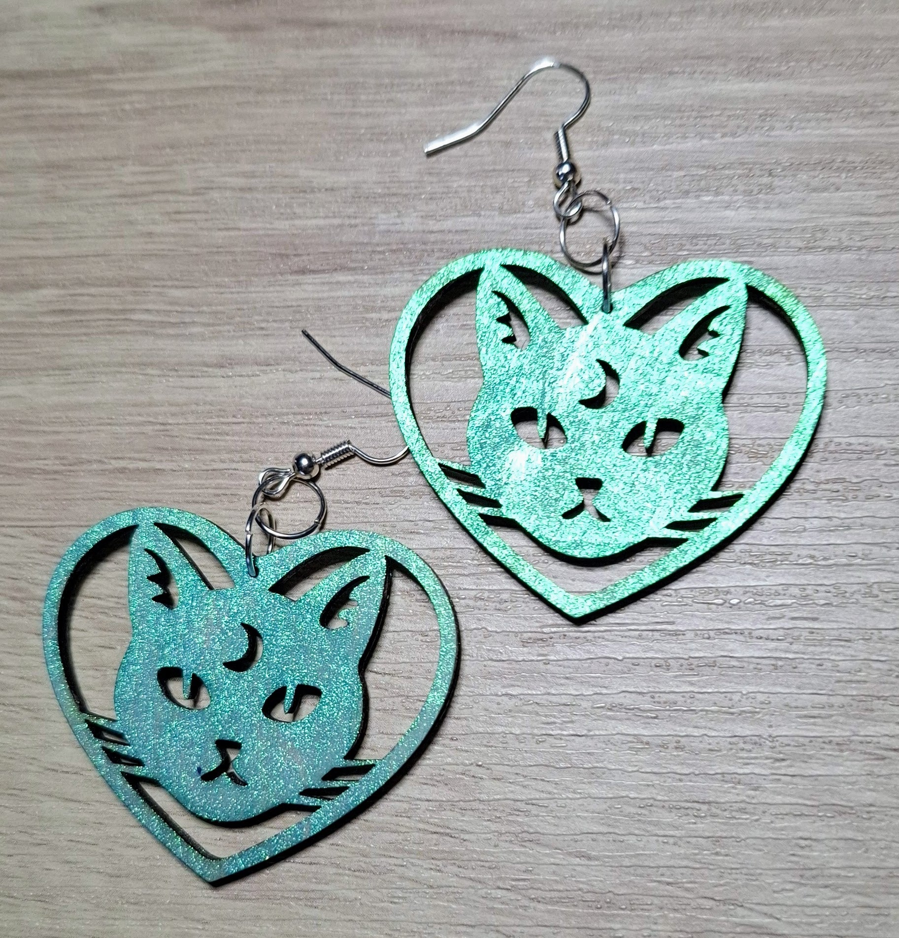 Teal cat-shaped earrings on a wooden surface