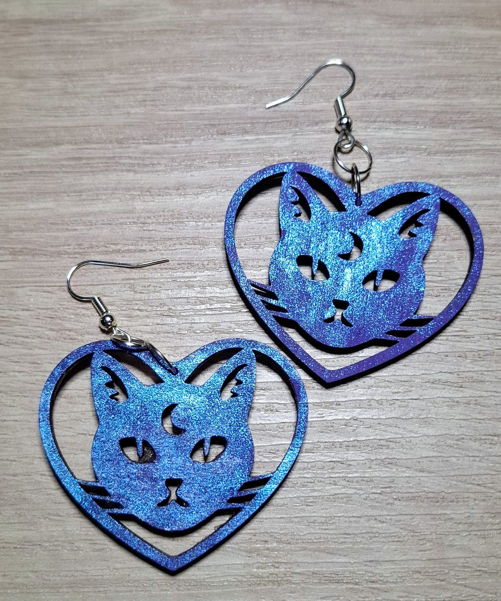 purple glittery cat-shaped earrings on a wooden surface