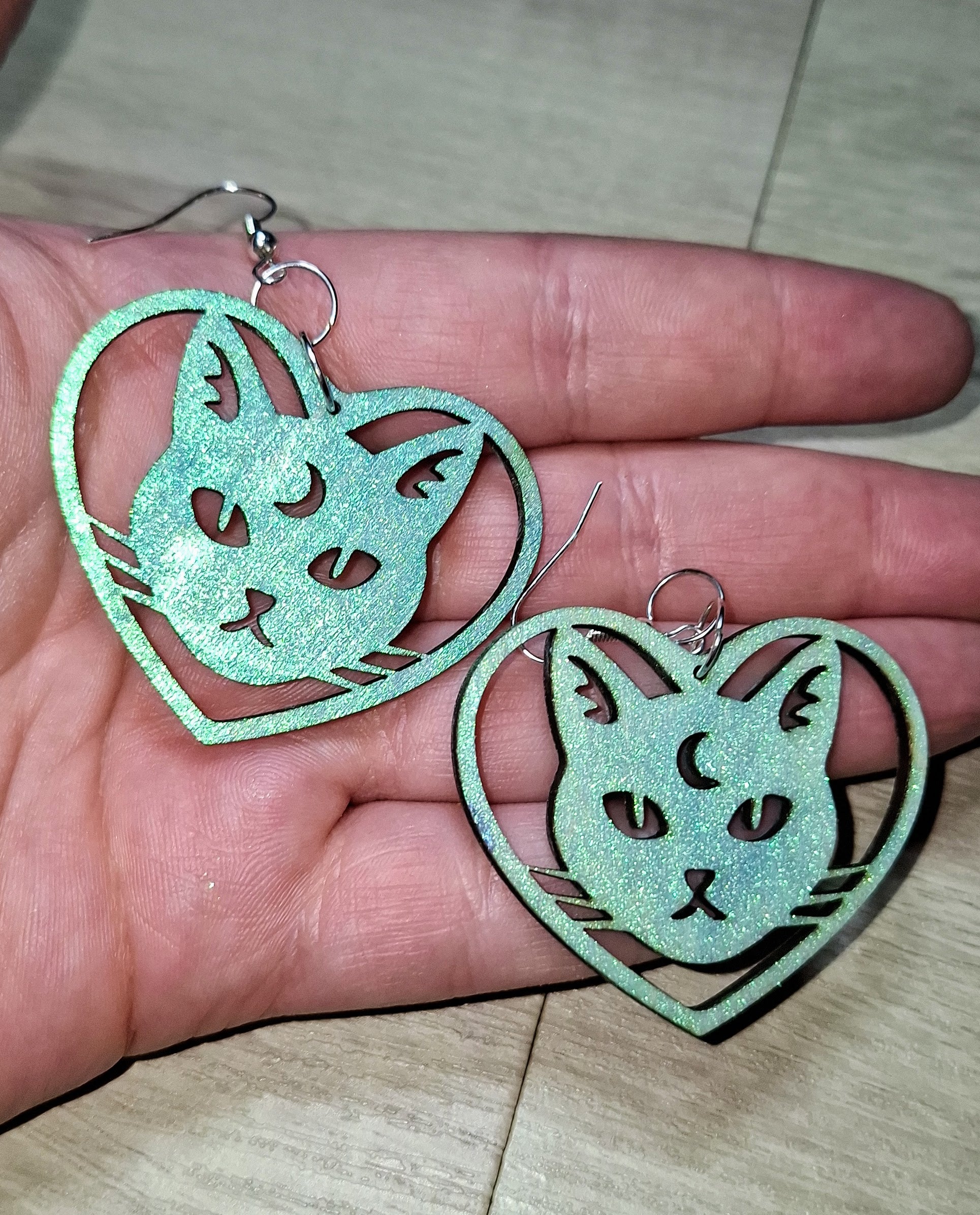 Turquoise cat-shaped earrings held in a hand on a light wooden surface