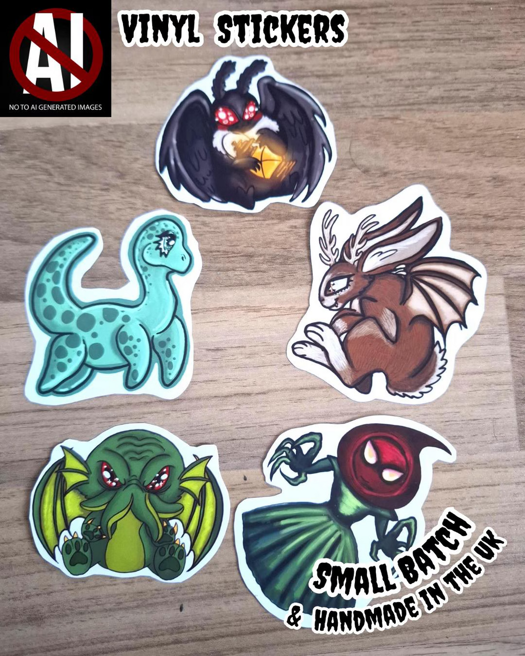 Five colourful vinyl stickers of cartoonish cryptids on a wooden surface with 'Small Batch & Handmade in the UK' text.