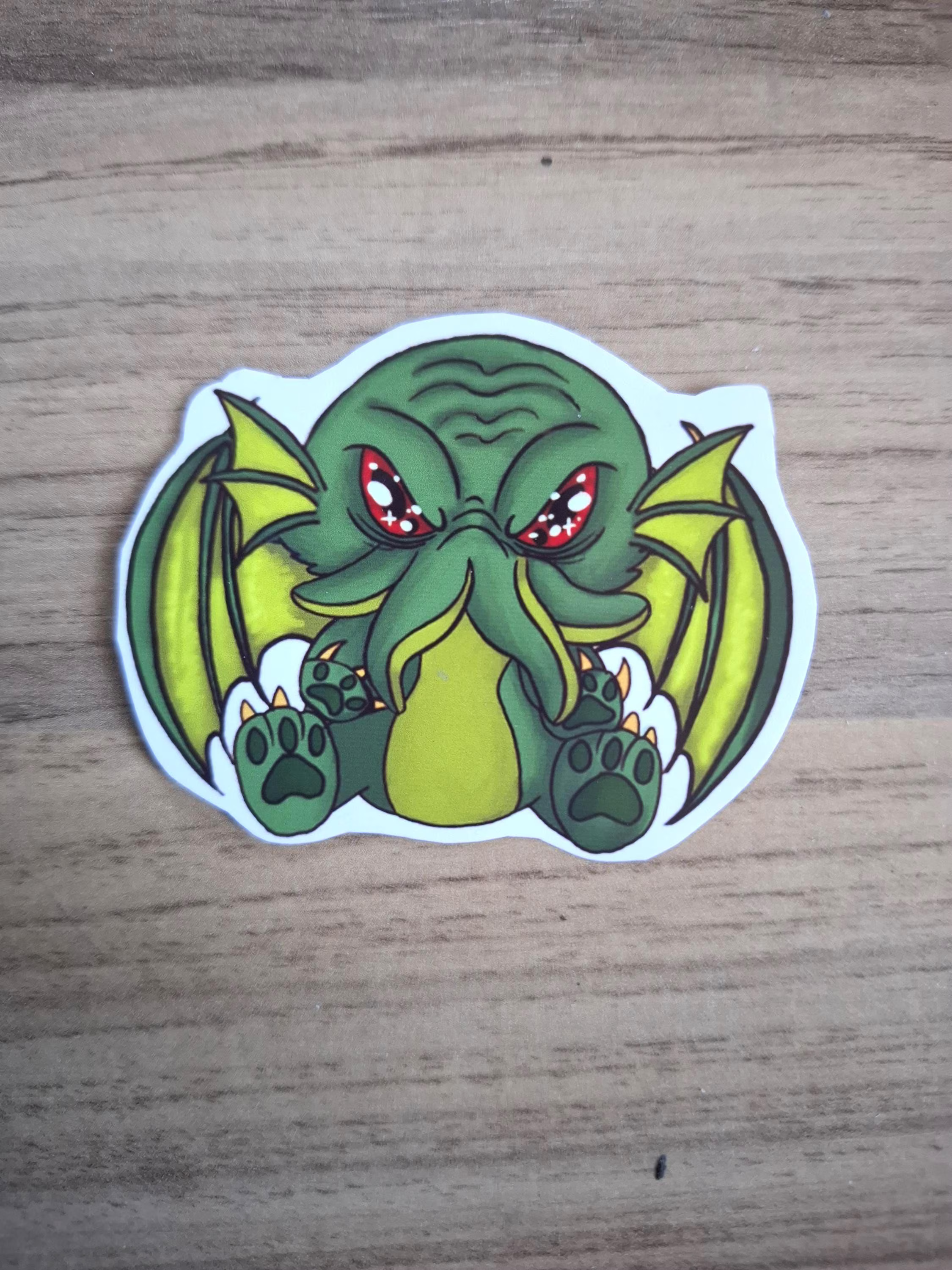 Cartoonish green creature sticker with red eyes on a wooden surface
