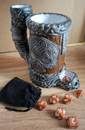 Decorative skull-themed cup with dice and a black pouch on a wooden surface