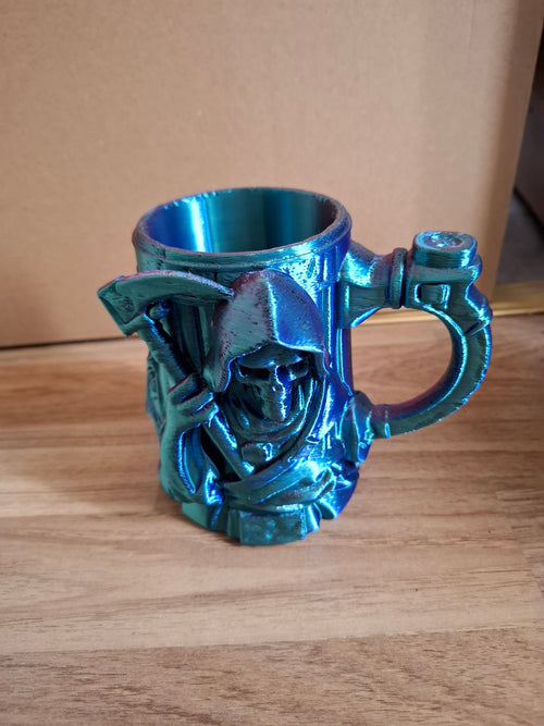 Metallic colourshifting decorative cup with 3d grim reaper design  on a wooden surface