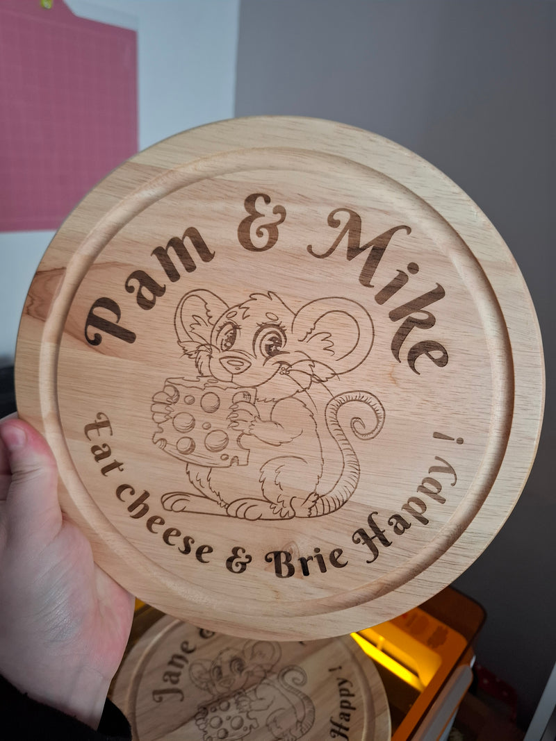 Wooden round chopping board with engraved text and a Mouse illustration, held by a hand.