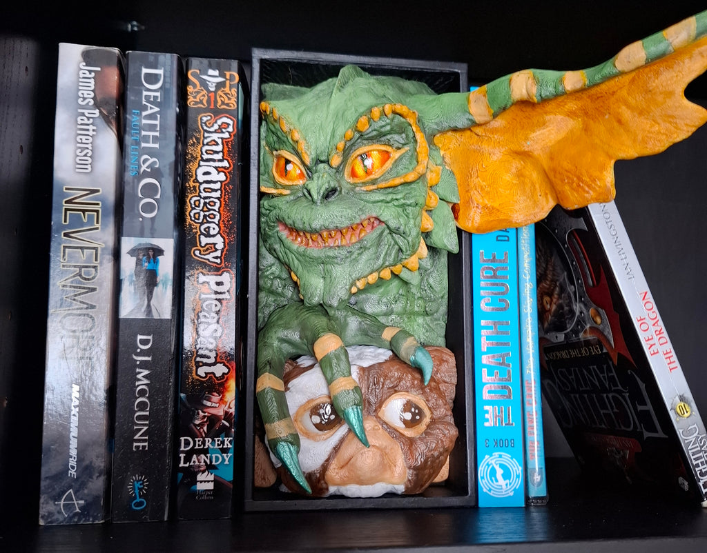 Decorative bookend shaped like a green gremlin and brown grelin on a shelf with books.