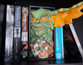 Decorative bookend shaped like a green gremlin and brown grelin on a shelf with books.