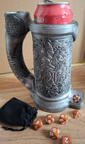Decorative beer mug with intricate designs, a can on top, and dice on a wooden surface.