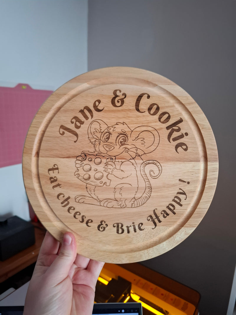 Wooden round cutting board with engraved text & mouse artwork and design, held by a hand.