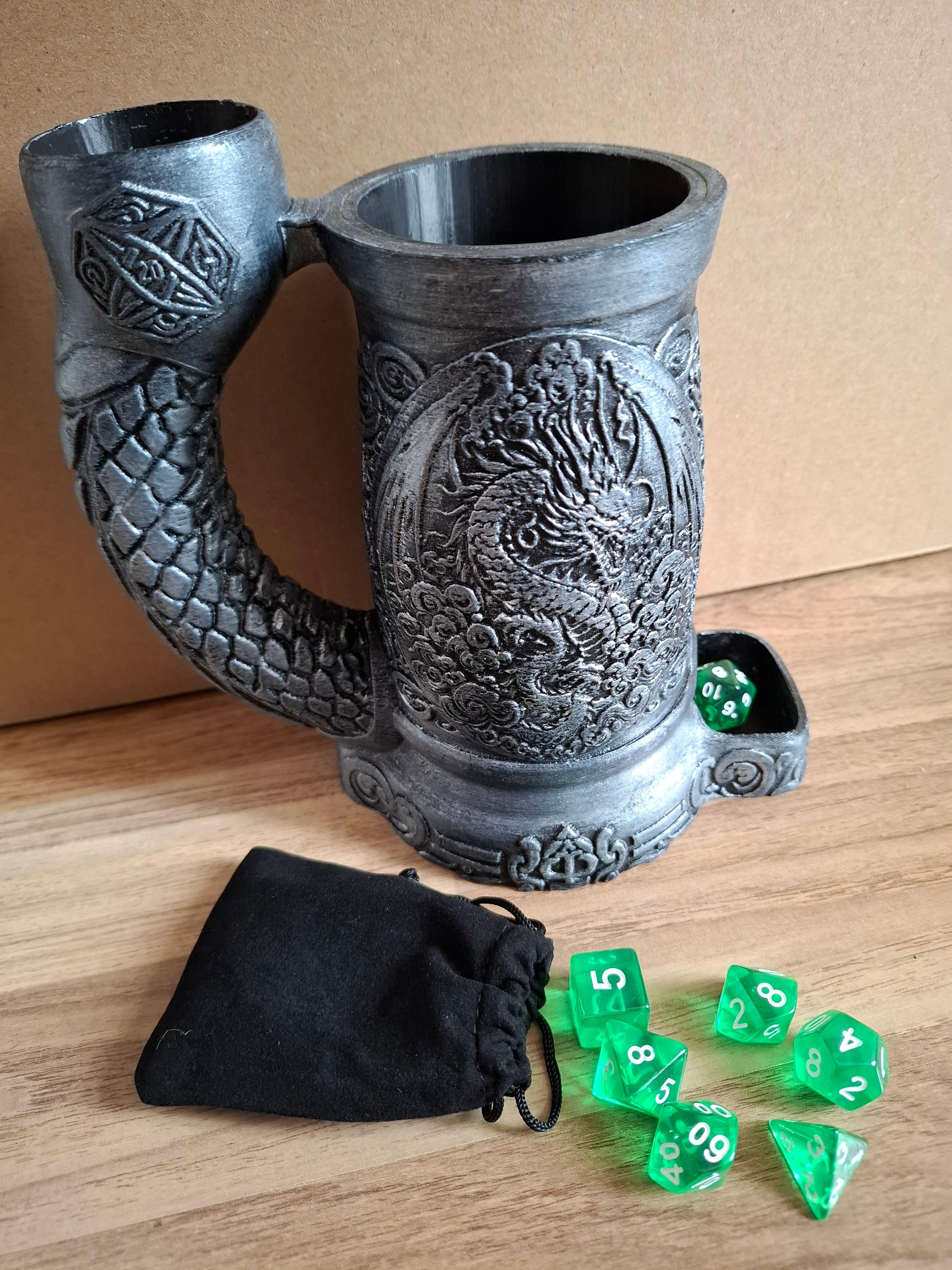 Decorative metal effect with dragon design dice cup with green dice and a black bag on a wooden surface